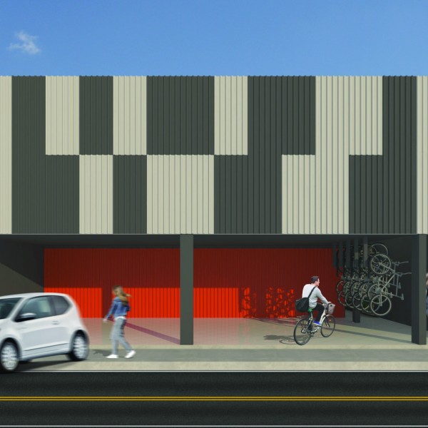 Vista da fachada frontal onde foi proposto um painel de telhas metálicas com interessante apelo visual, criado pela alternância de telhas pretas e galvanizadas, no segundo plano optou-se pela telha vermelha. Outro ponto importante de ressaltar é o espaço destinado ao bicicletário, ao lado das vagas cobertas destinadas aos clientes. (Ar:Co – Arquitetura Cooperativa).